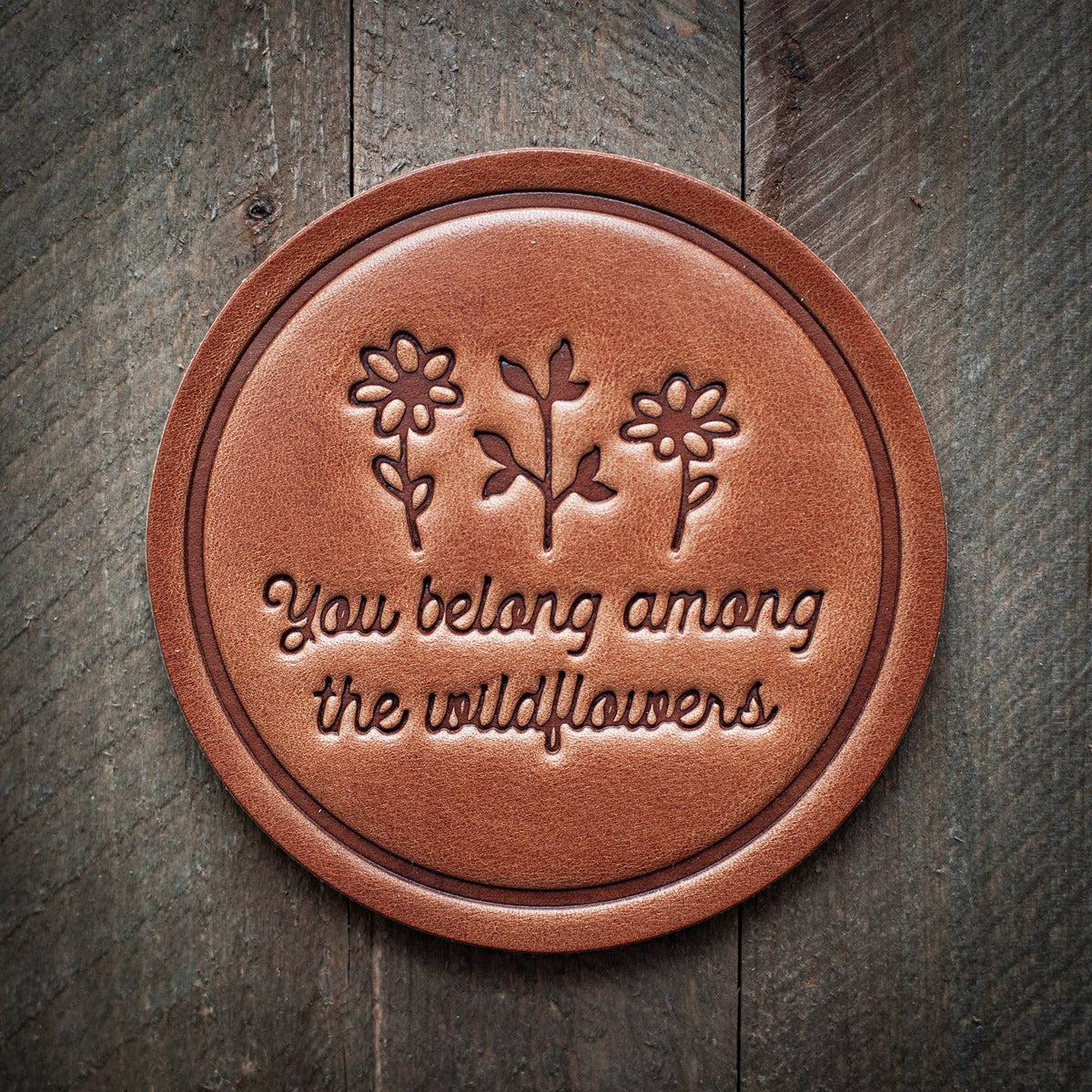 Handmade round leather coaster with embossed wildflowers and "You belong among the wildflowers" text, artisan gift-quality. - You Belong Among the Wildflowers Leather Coaster
