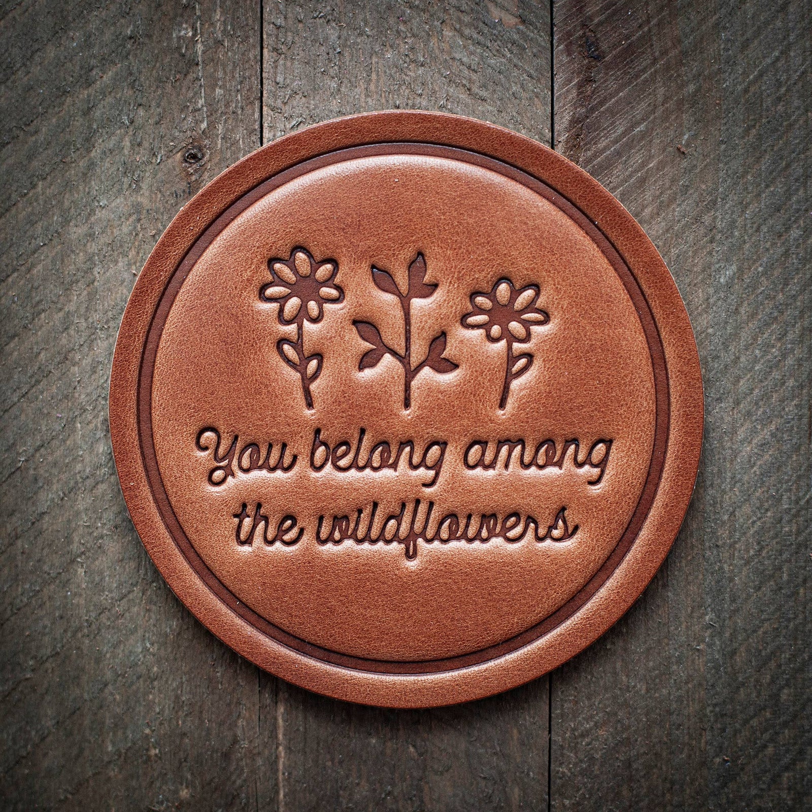 Handmade round leather coaster with embossed wildflowers and "You belong among the wildflowers" text, artisan gift-quality. - You Belong Among the Wildflowers Leather Coaster