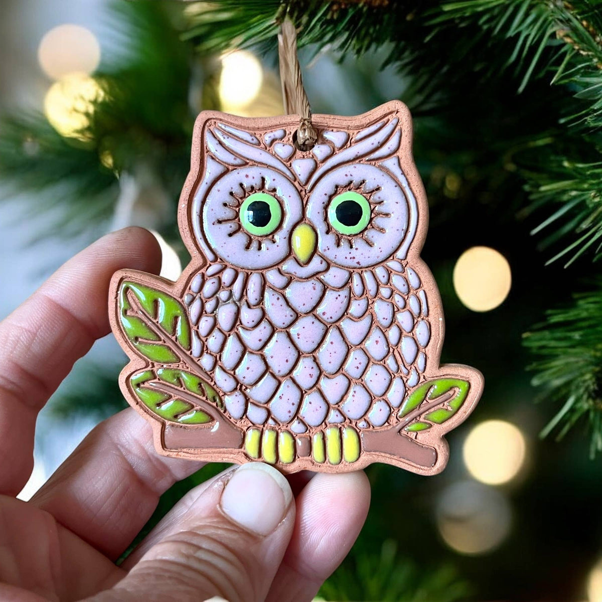 Decorative owl ornament held in front of a Christmas tree with lights.
