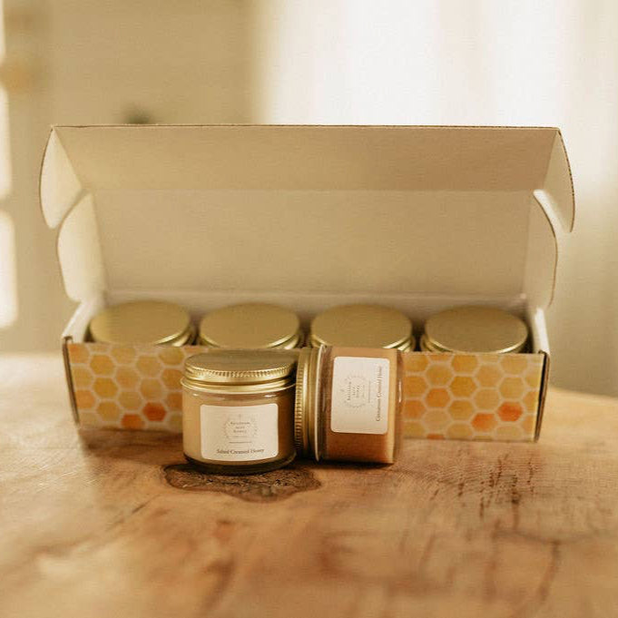 Two jars of creamed honey sits in front of a gift box with a label that reads 'Salted Honey'. The box contains more bucks county local honey in a sample size gift set.