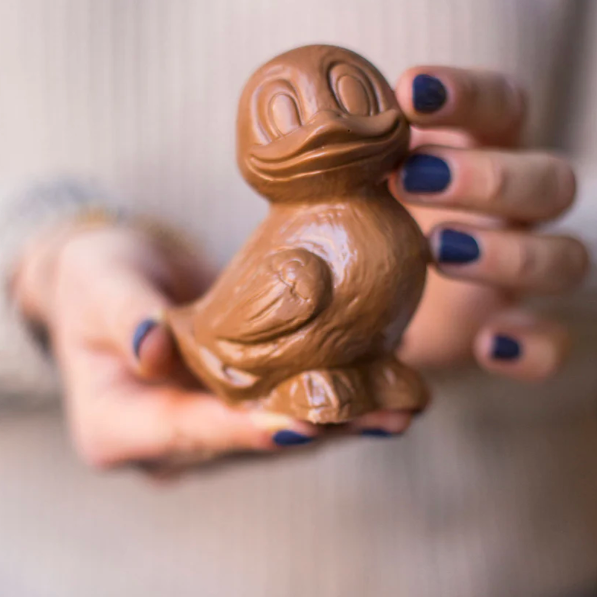 Chocolate duck-shaped object held in a hand with blue nail polish against a blurred background