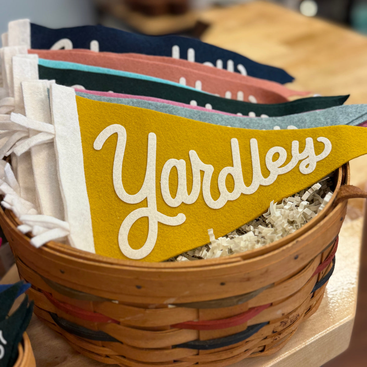 Basket with colorful pennants, including one with 'Yardley' text, on a wooden surface.