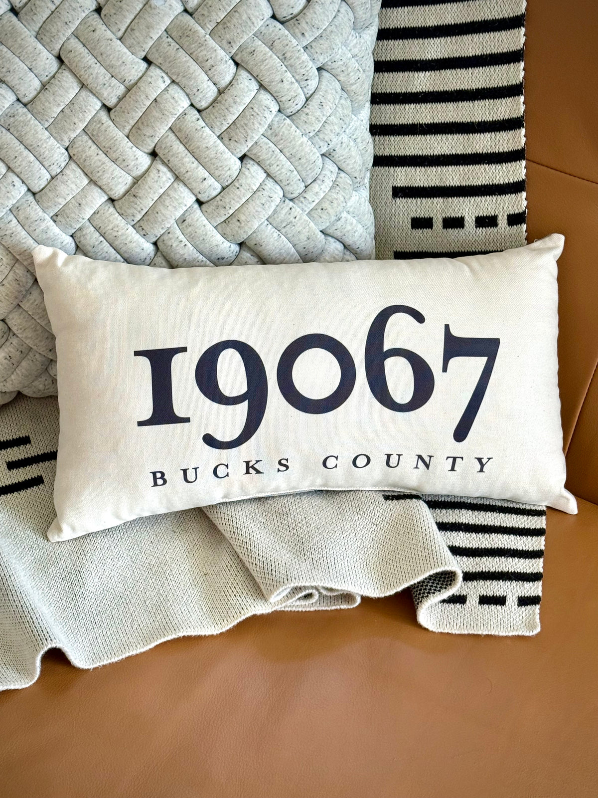Decorative pillow with '19067 Bucks County' text on a textured surface.