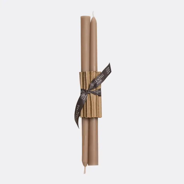 Two tall taper candles in a warm taupe-brown color, wrapped together with a textured gold paper band and a dark brown ribbon printed with the brand name 'Candlelight'.