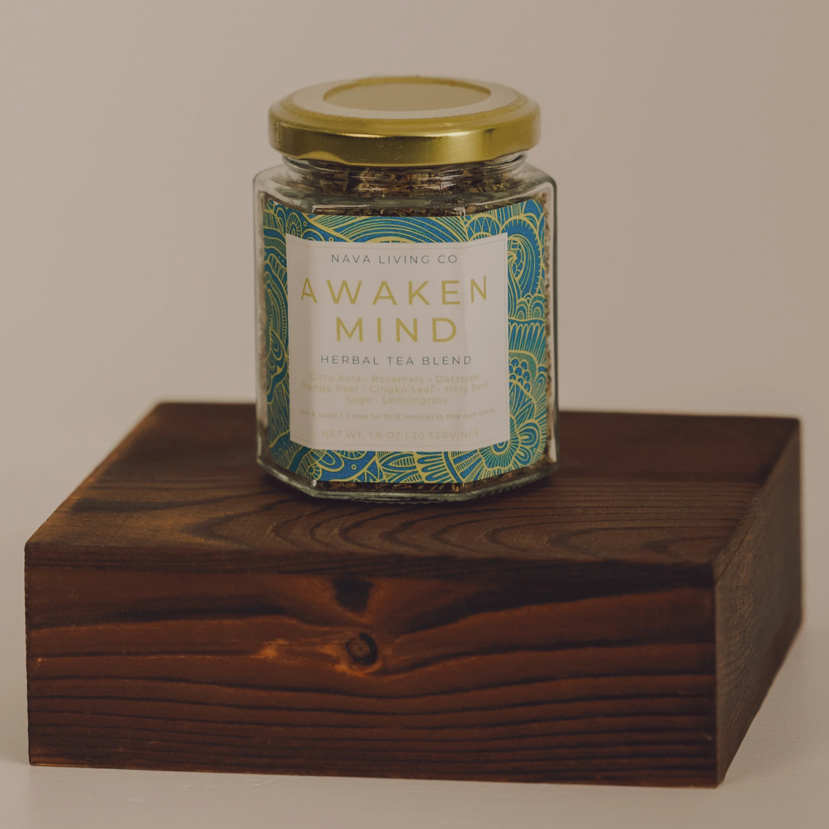 Jar of 'Awaken Mind' herbal tea blend on a wooden block with a neutral background