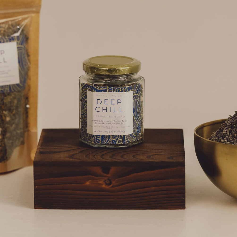Jar labeled 'Deep Chill' herbal tea with a wooden block and gold bowl containing dried herbs on a neutral background