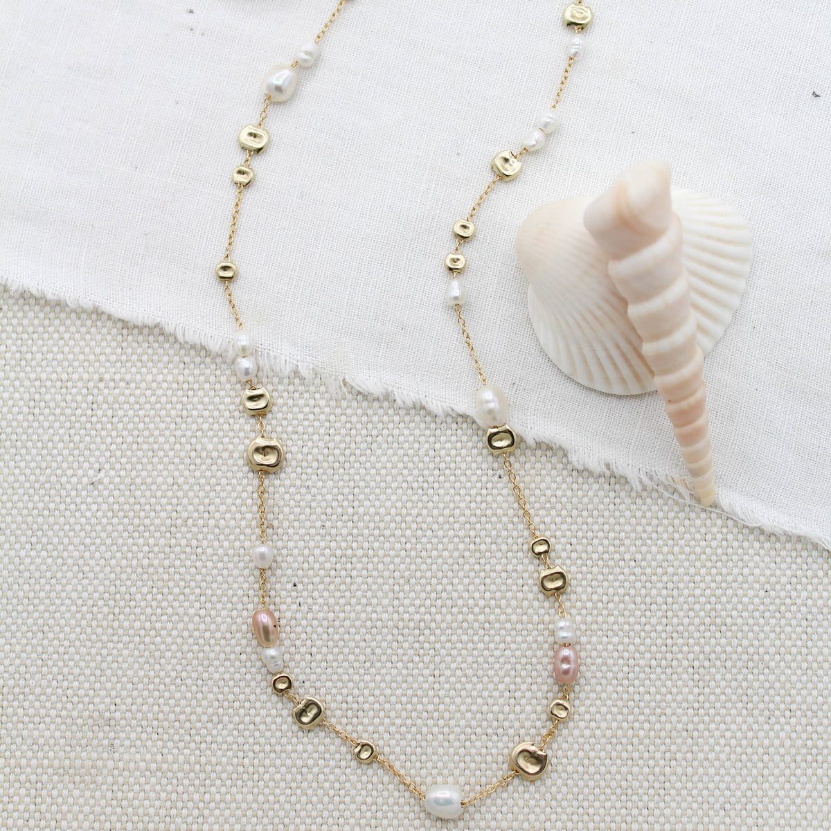 Necklace with gold and pearl beads on a textured fabric background