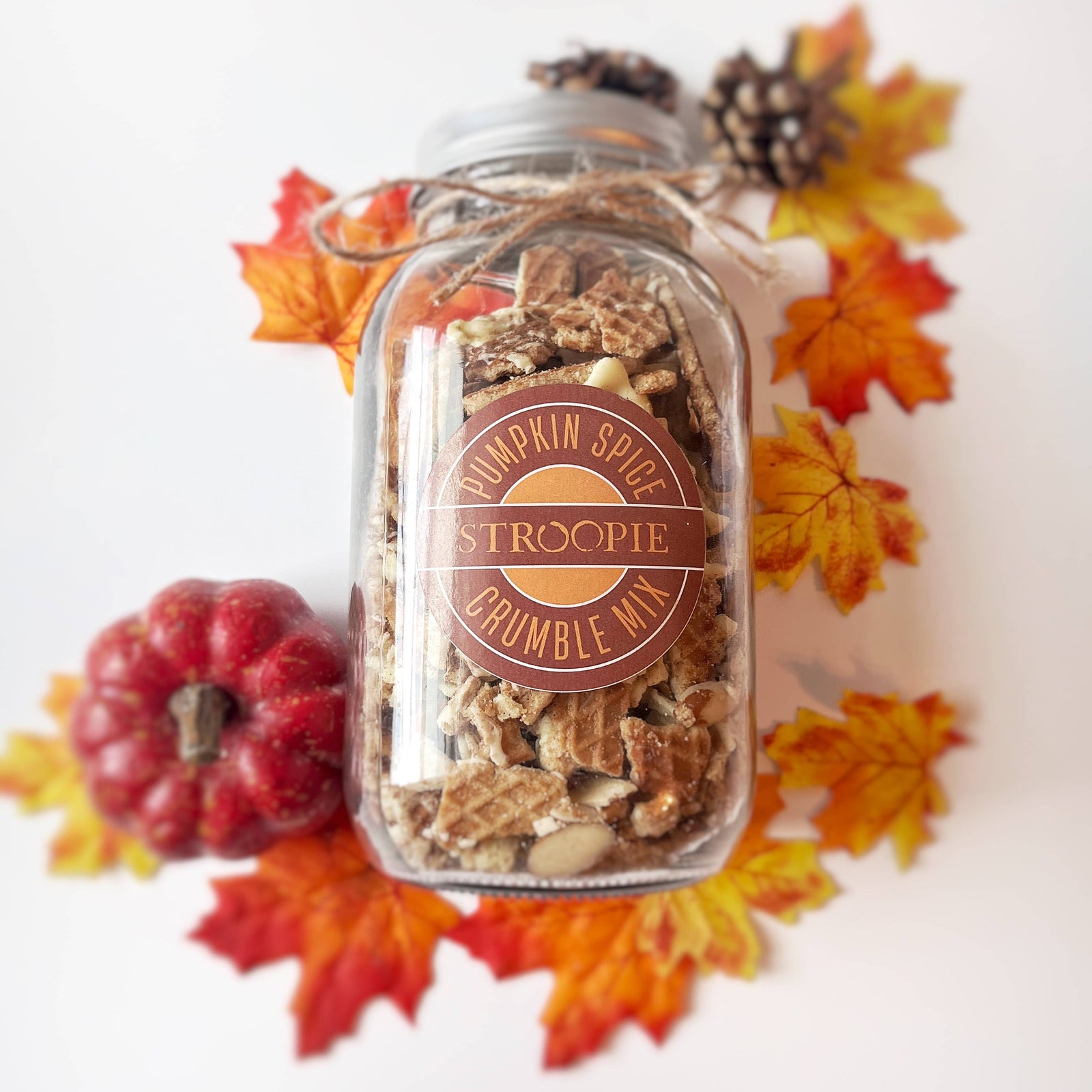 Jar of pumpkin spice crumble mix with decorative fall leaves and a small pumpkin on a white background