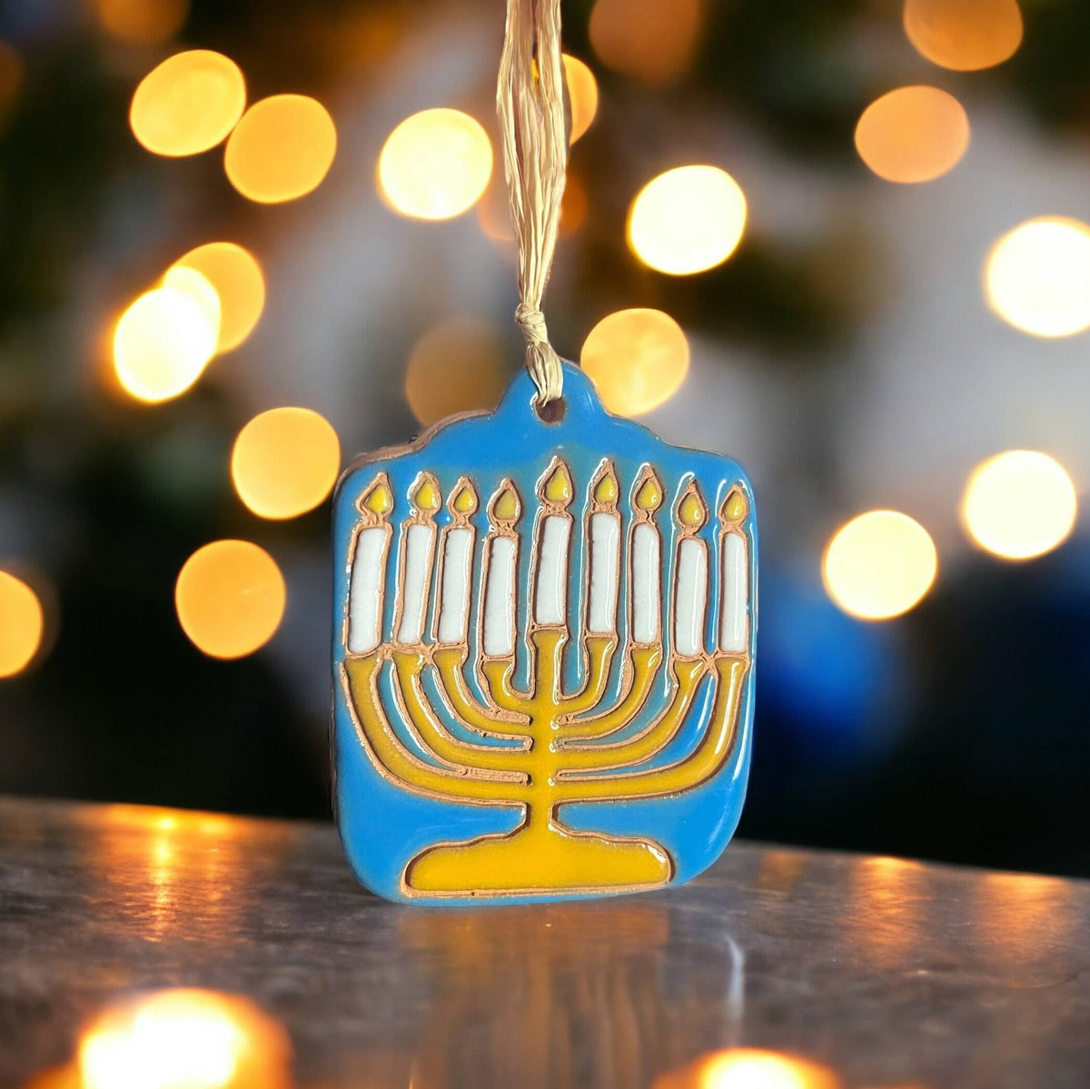 Decorative Menorah ornament on a reflective surface with blurred lights in the background