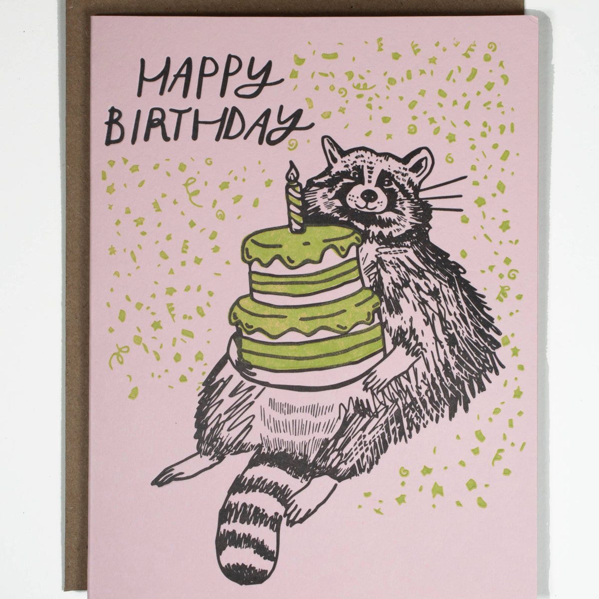 Handmade birthday card with unique raccoon illustration holding green cake on pink background. - Birthday Raccoon Card