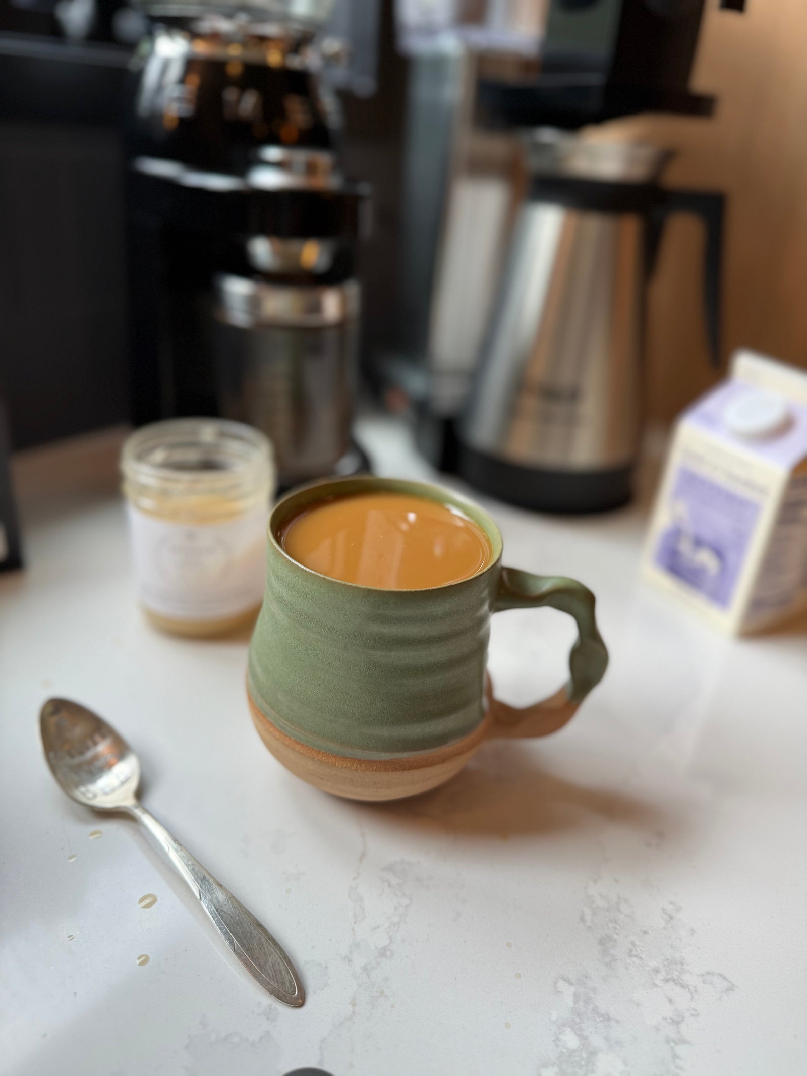 a handcrafted mug serves morning coffee next to a fun vintage spoon, honey, creamer and a coffee maker