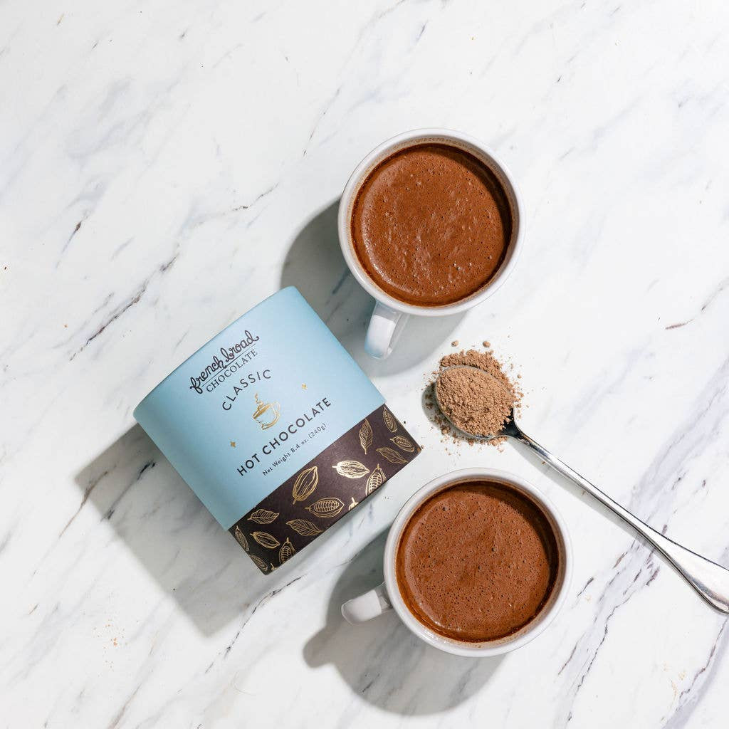 Two cups of hot chocolate with a container labeled 'Hot Chocolate' on a marble surface.