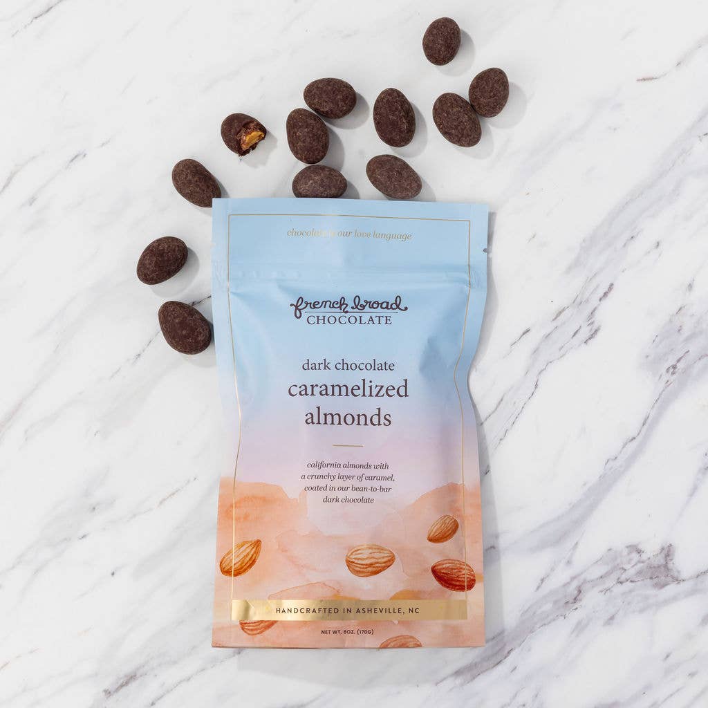 Package of French Broad Chocolate dark chocolate caramelized almonds on a marble surface with scattered almonds.