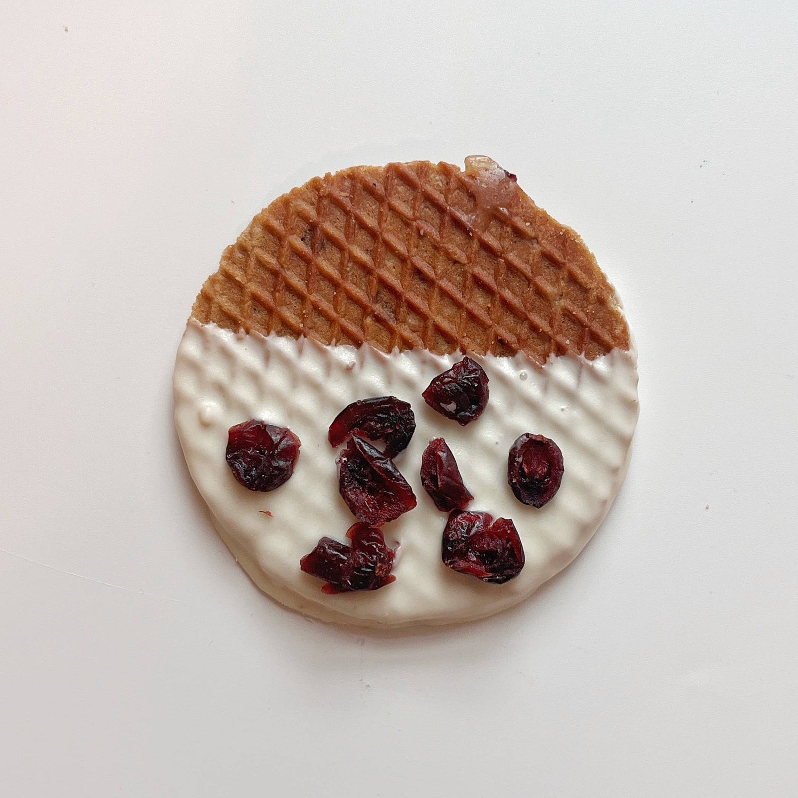 Round cookie with white chocolate coating and dried cranberries on a light background