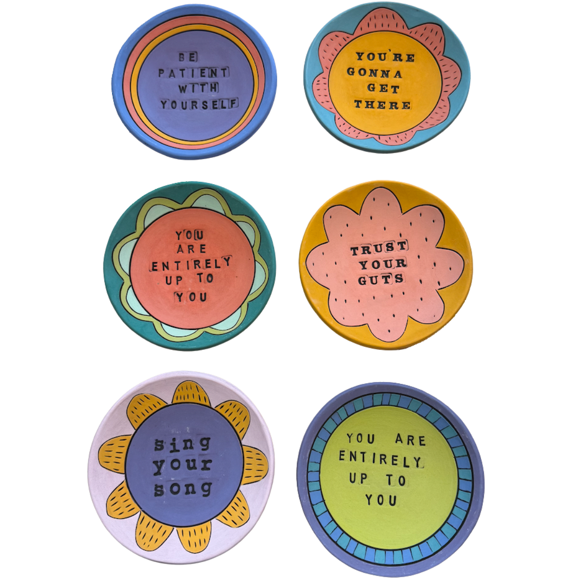 Six hand-painted terra cotta ring dishes arranged in a 2x3 grid on a white background, each featuring a different positive affirmation in black text inside a colorful, retro-style circular design.