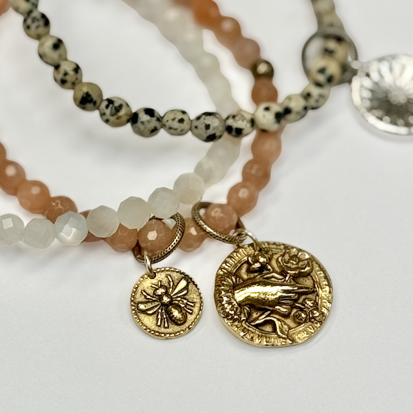 Stack of beaded bracelets with gold charms on a white background