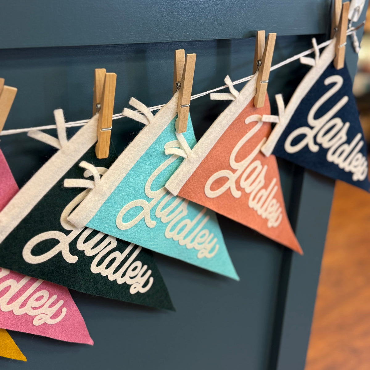 Colorful triangular flags with 'Yardley' text hanging on a line against a dark blue wall.