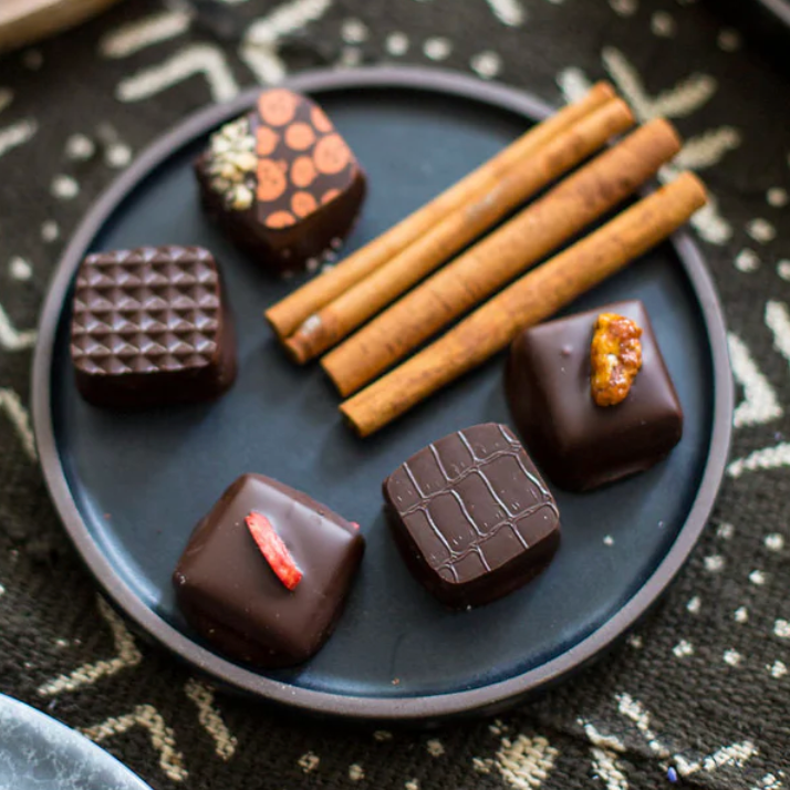 Assorted chocolate candies on a dark plate with cinnamon sticks on a patterned surface