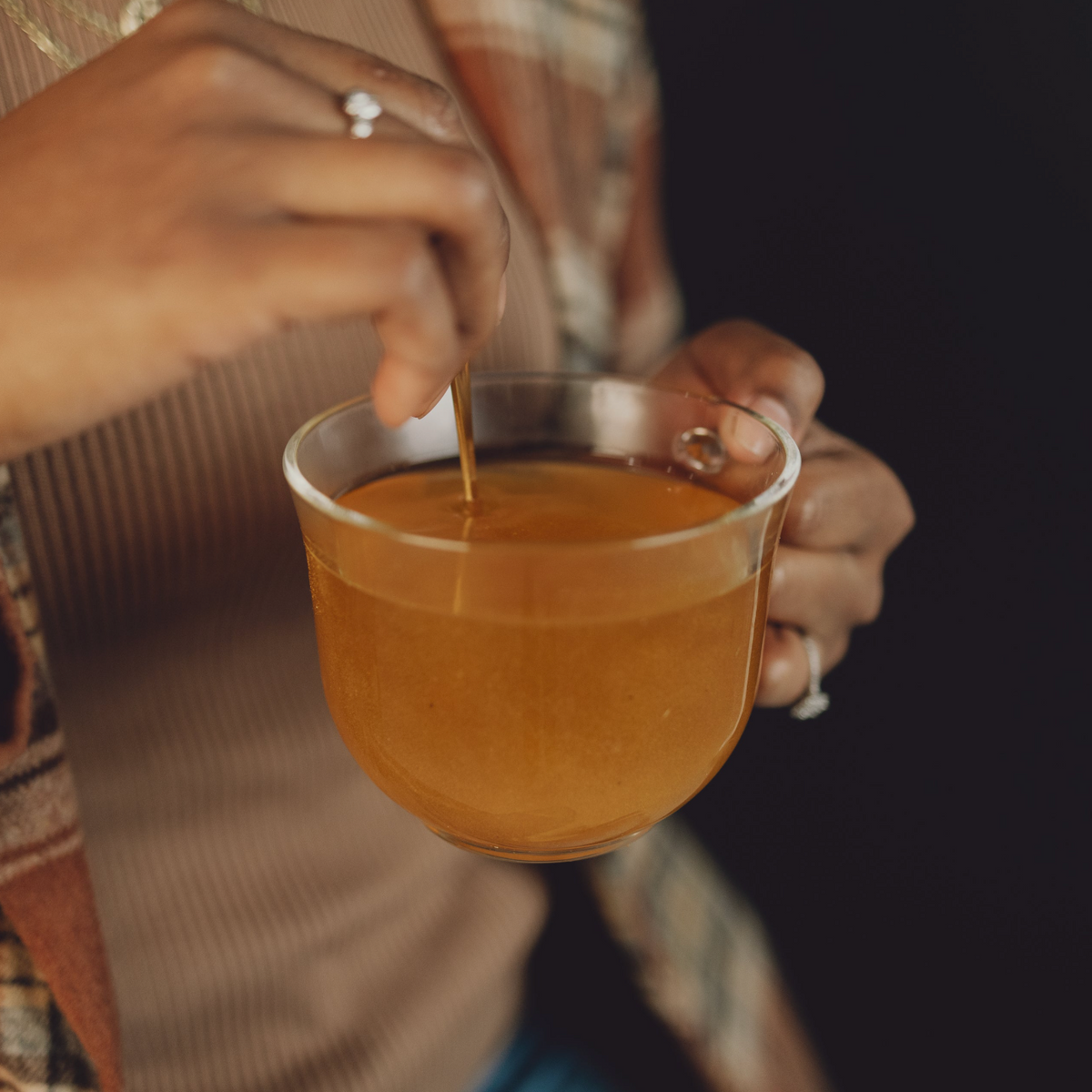 Person stirring a cup of tea with a spoon against a dark background