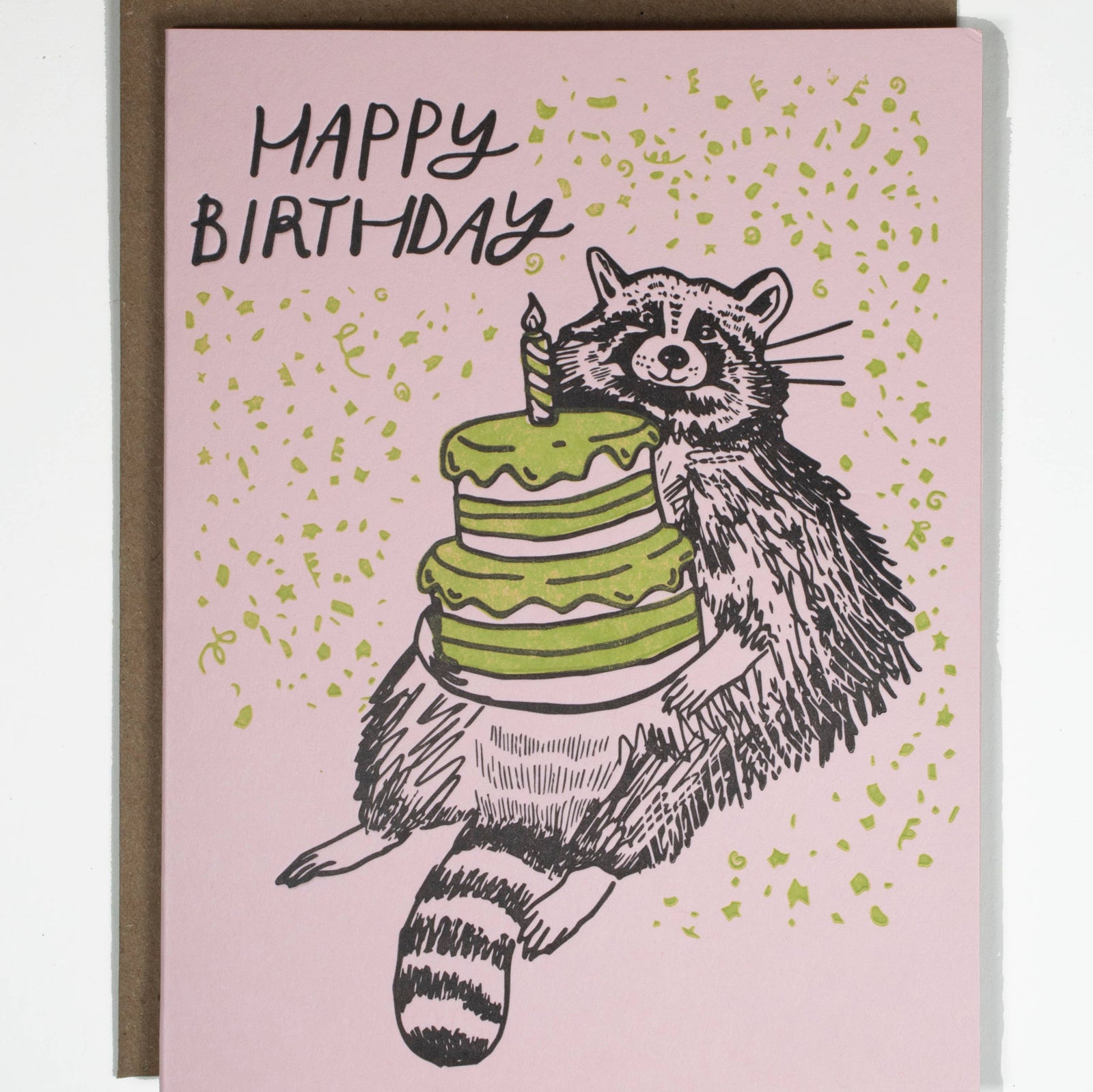 Handmade birthday card with unique raccoon illustration holding green cake on pink background. - Birthday Raccoon Card